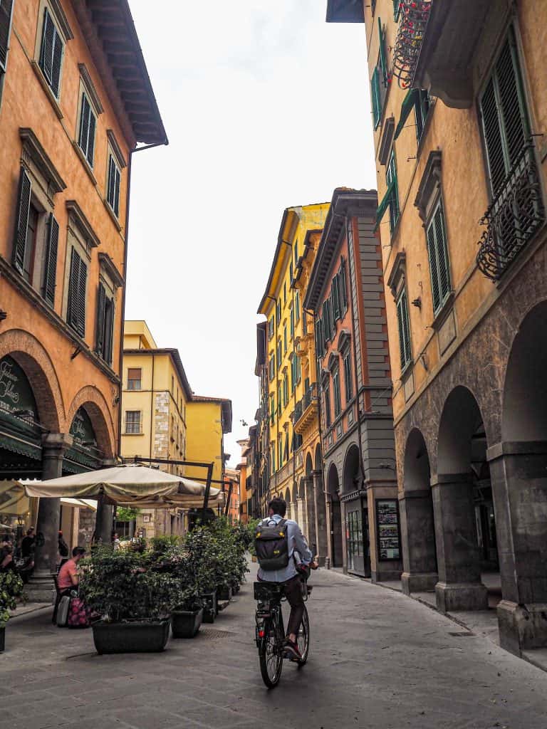 One day in Pisa: Man riding bike down a street with restaurant outdoor seating on the left
