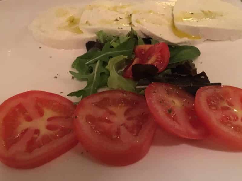 Sampling the fine dining scene in Florence A simple caprese salad with sliced red tomatoes, mozzarella in the back and rocket in the middle. The mozzarella has a drizzling of olive oil. At Il Barretto