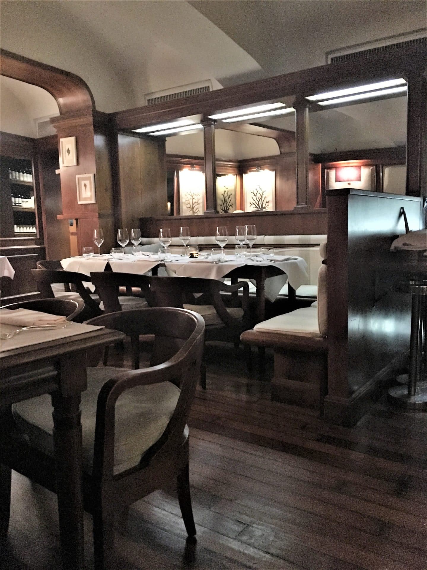 The interiors of Il Barretto Restaurant. Chairs and tables with white table cloths upon which are empty wine glasses.