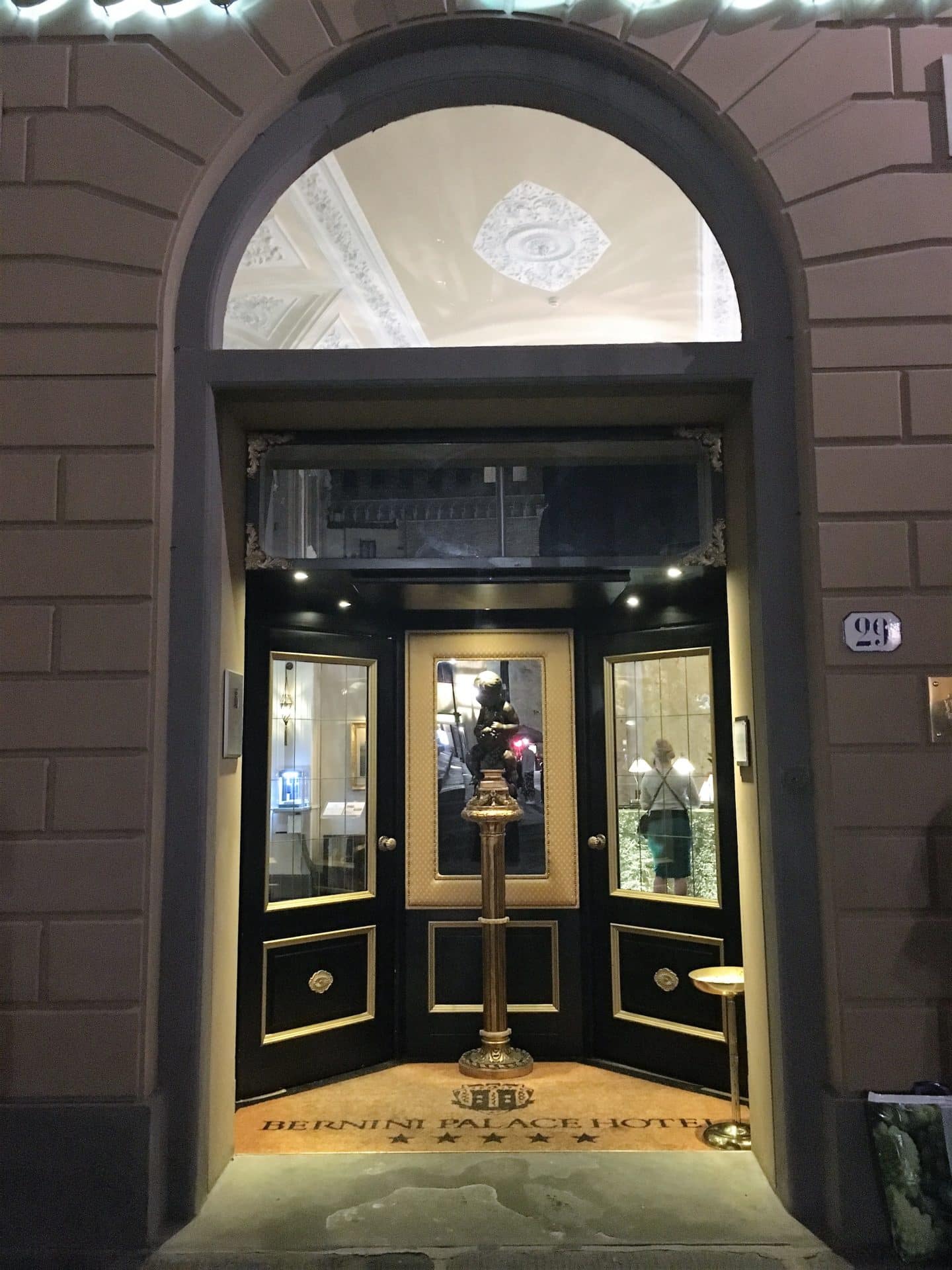An opulent stay at The Bernini Palace Hotel, Florence The Opulent Bernini Palace Hotel front door which is dark and split into three walkways. The door is glass and set into the beige stone work of the building. There is a tall flower vase in front of the door, the lights are shininhg through the door