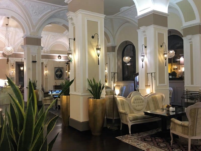 An opulent stay at The Bernini Palace Hotel, Florence White and beige arches inside Bernini Palace hotel wit french-style seating, tables and down lighters. Scattered throughout the space are a metre high gold vases with green plants