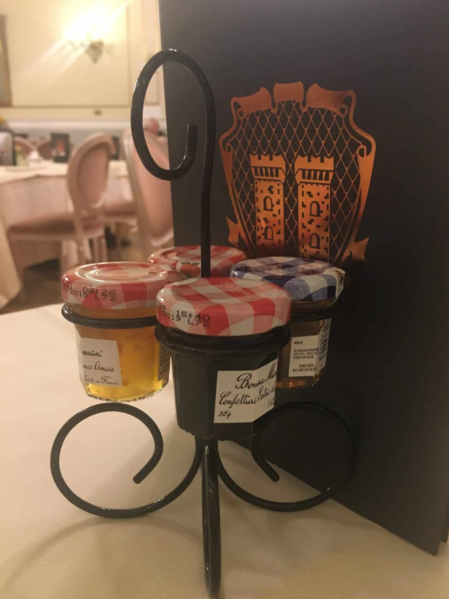 An opulent stay at The Bernini Palace Hotel, Florence An opulent stay at The Bernini Palace Hotel, Florence. Black wire conserve holder with 4 mini bottle sof jam and marmalade with a dark brown covered Breakfast menu in the background.