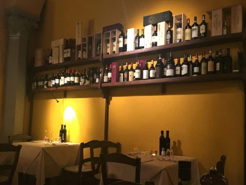 Sampling the fine dining scene in Florence The yellow wall interiors of Parione adn on the shelves are bottle sof wine. Underneath them are 2 tables with olive oil adn balsamic vinegar.