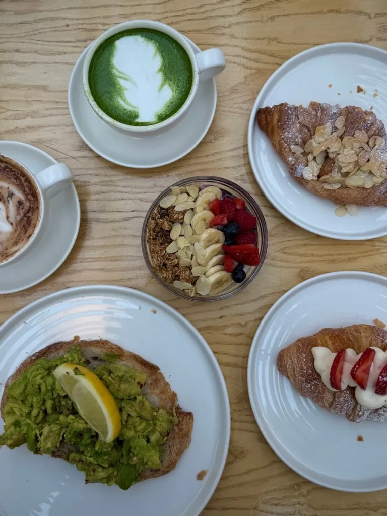 Flat lay of matcha, almond croissant, cappuccino, berry compot, avocado toast and an almond croissant at Public & Plants in Leicester
