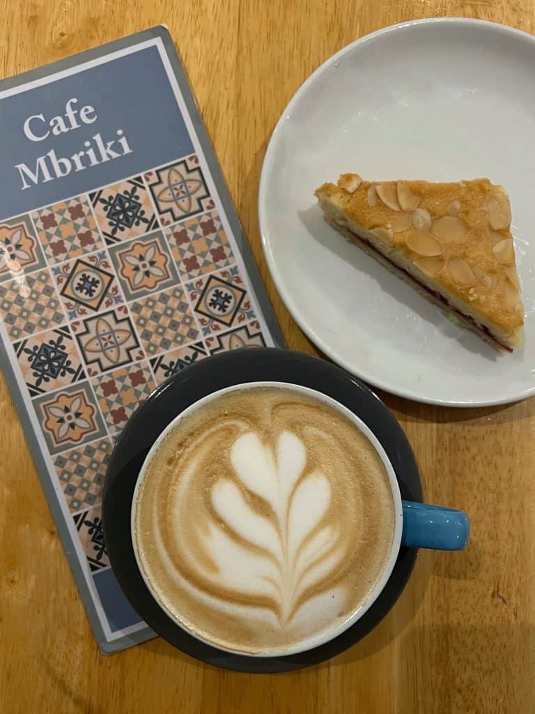 Flatlay of a latte with coffee art, a cafe Mbriki menu and an almond and black cheery slice, Leicester