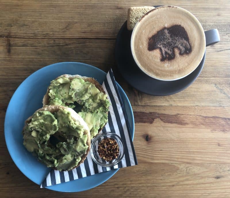 Independent Coffee Shops in LE1, Leicester. Top lay of a mocha with a bear chocolate stencil. There is a bagel topped with Avocado and chilli flakes and a striped napkin on a blue plate at Orso cafe