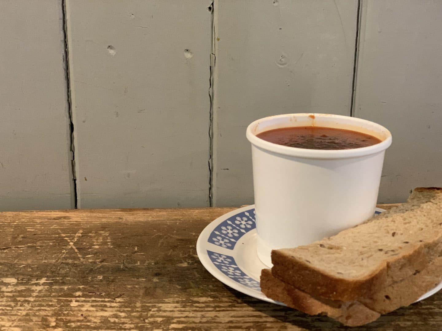 Independent Coffee Shops in LE1, Leicester. Tomato and basil soup in a paper cup with a slice of brown bread on a plate in Bread & Honey cafe.