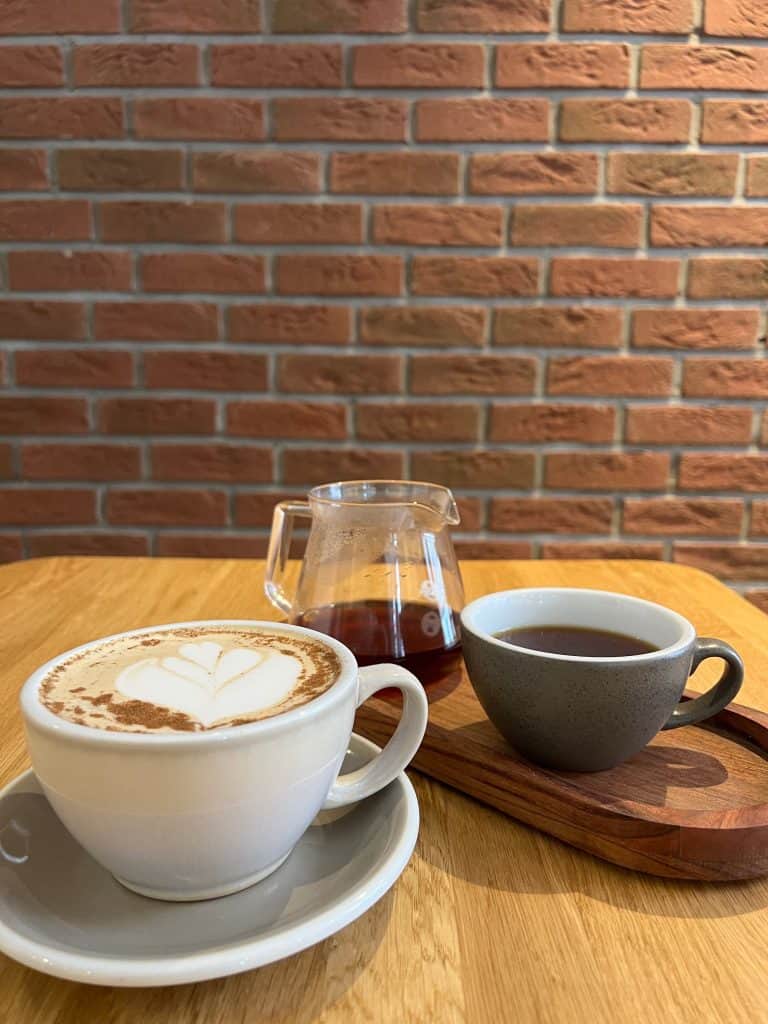 Cappuccino and black filter coffee against a brick wall in Saints of Mokha