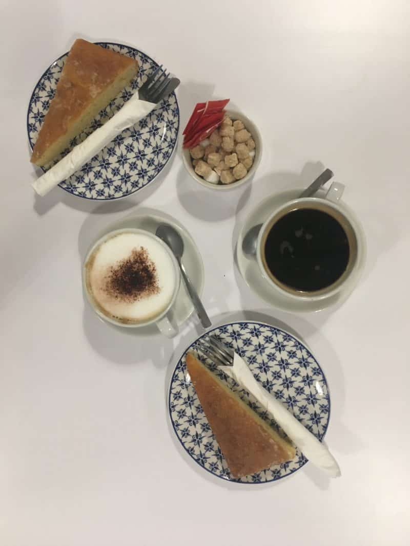 LE1:Independent Coffee & Cake Locales Grays Coffee shop and Kitchen Cappuccino and black coffee with 2 slices of cake on blue and white plates. Flatlay photograph. Coffee shop location is in Leicester
