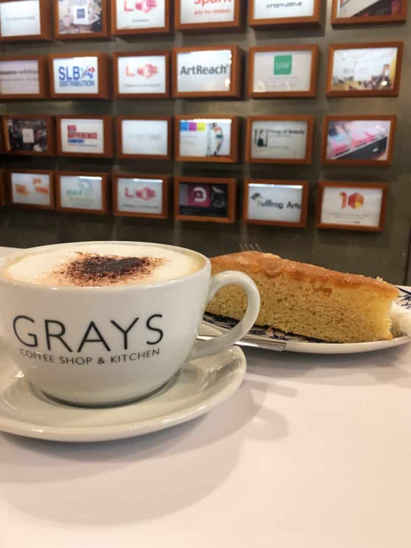 LE1:Coffee & Cake Locales Grays Coffee shop and Kitchen, Leicester. Cappuccino cup with Grays on the side and a slice of cake with Business cards in the background.