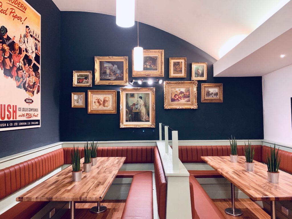 The interiors of Five Fox Lane cafe in Leicester, The walls are blue and whte and there are eclectic photos on them with diner style seatings and brown wooden long tables.