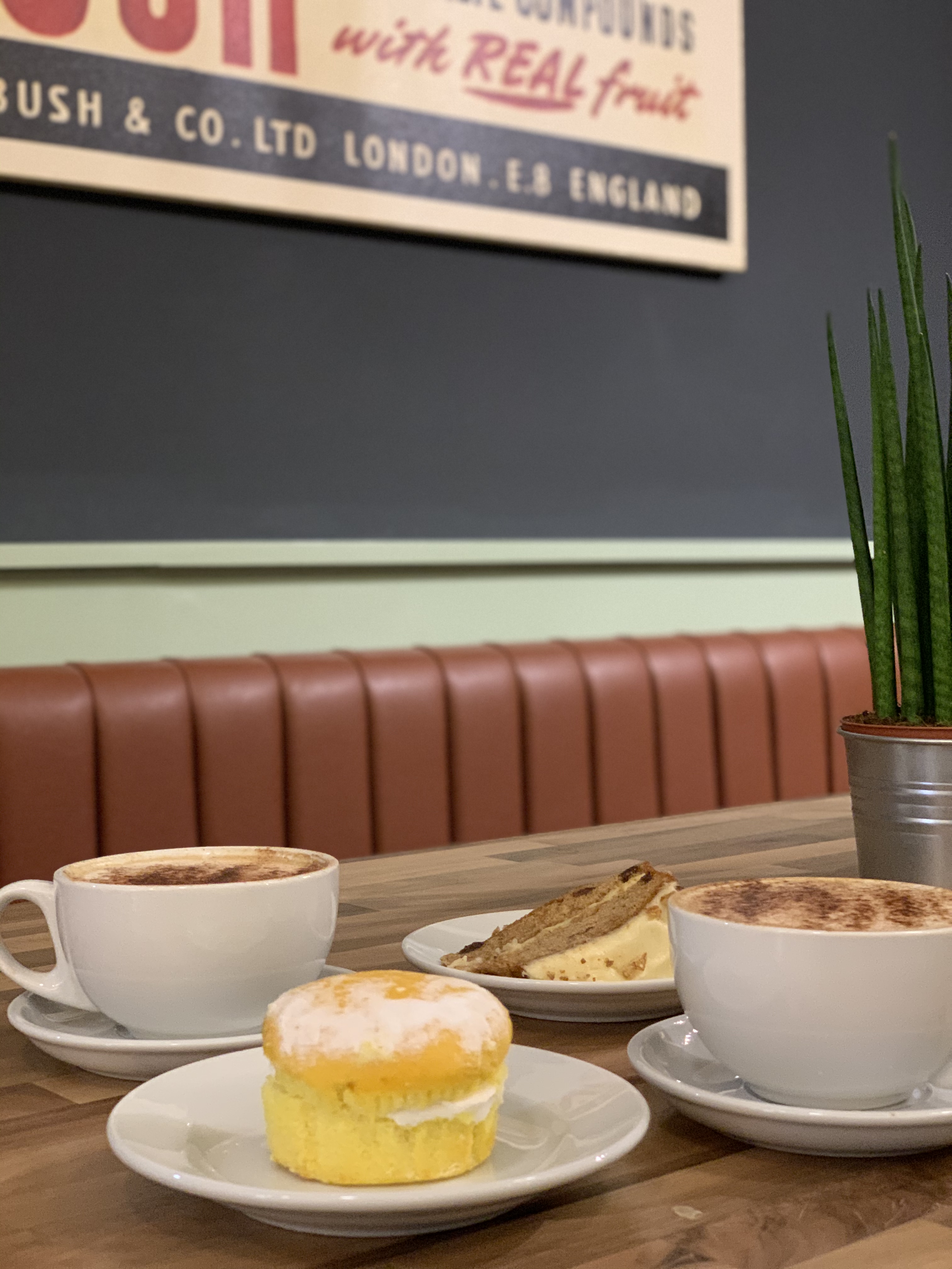 Five Fox Lane Coffee Shop, Leicester. 2 coffees in white cups with a green cactus plant in a silver pot. There is a slice of cake and a mini Victoria sandwich.
