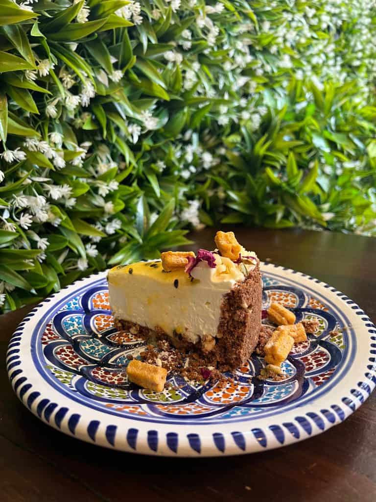 Cheesecake on a plate in front of a flower and leaf wall at La Foret Cafe