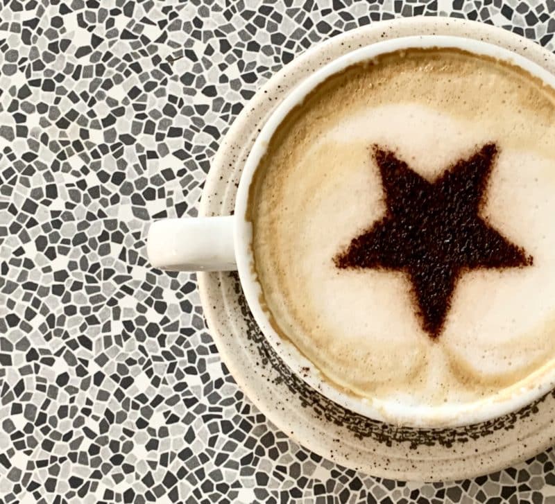 Independent Coffee Shops in LE1, Leicester. A cappuccino with a chocolate star stencil on a speckled black adn white table at Bryter Moon deli.