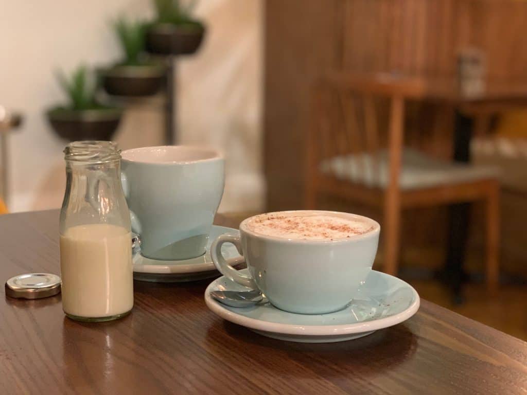 Latte in a duck egg clue cup with a black coffee and a small bottle of milk at Black Iron Social, Leicester