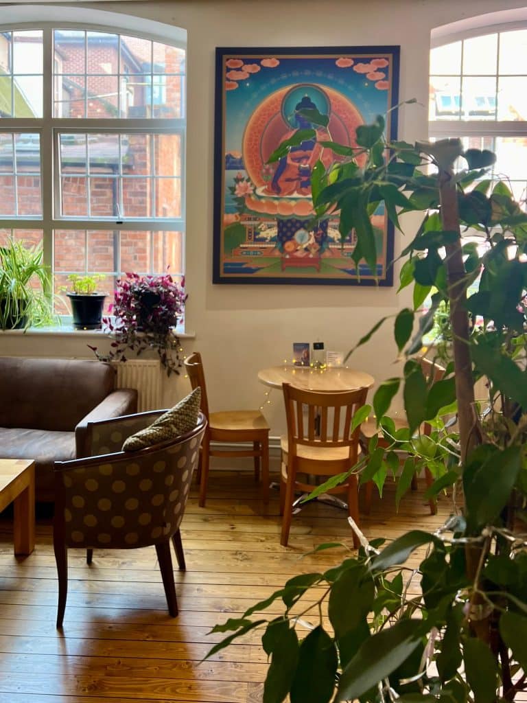 2 large windows with a table, chairs and sofe infront of them. There are plants and photos on the walls.