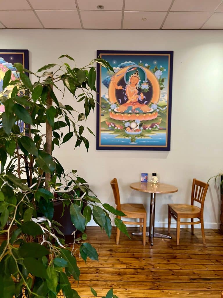 A table with 2 chairs at the World Peace Cafe with a meditation photo hanging on the wall and a plant to the left hand side