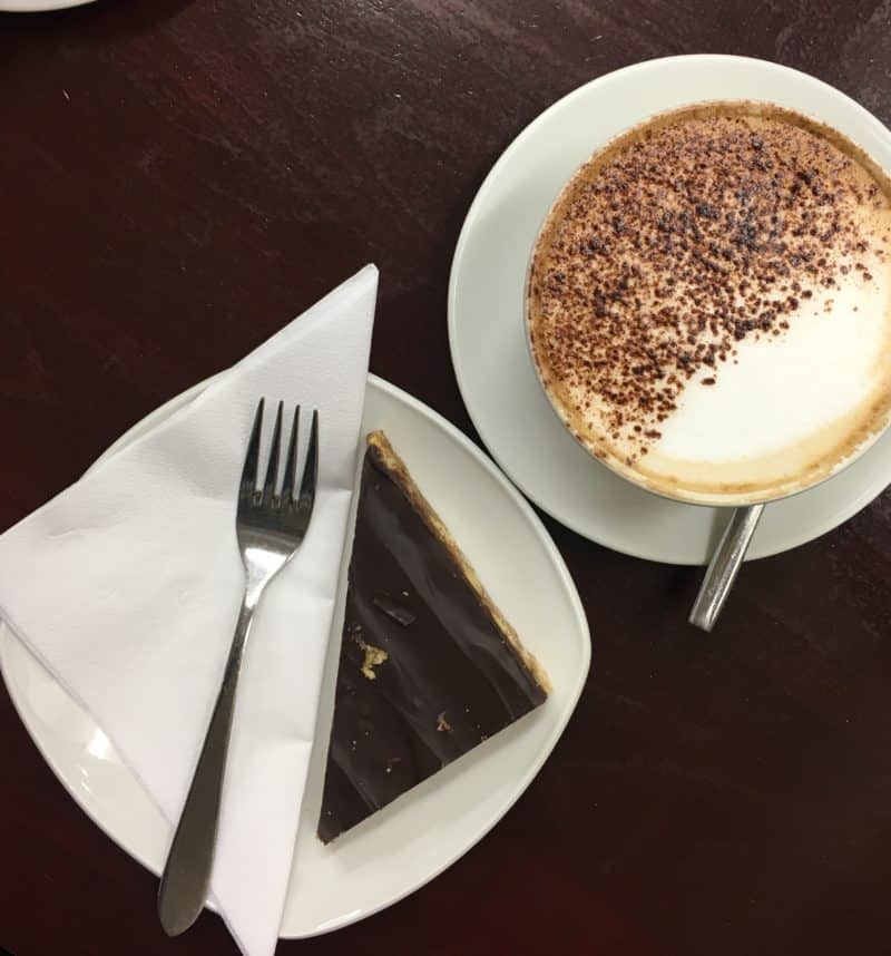 LE1 Coffee & Cake Locales Cafe Dido. Half chocolate dusted cappuccino with a caramel slice topped in chocolate with a fork adn napkin in Leicester