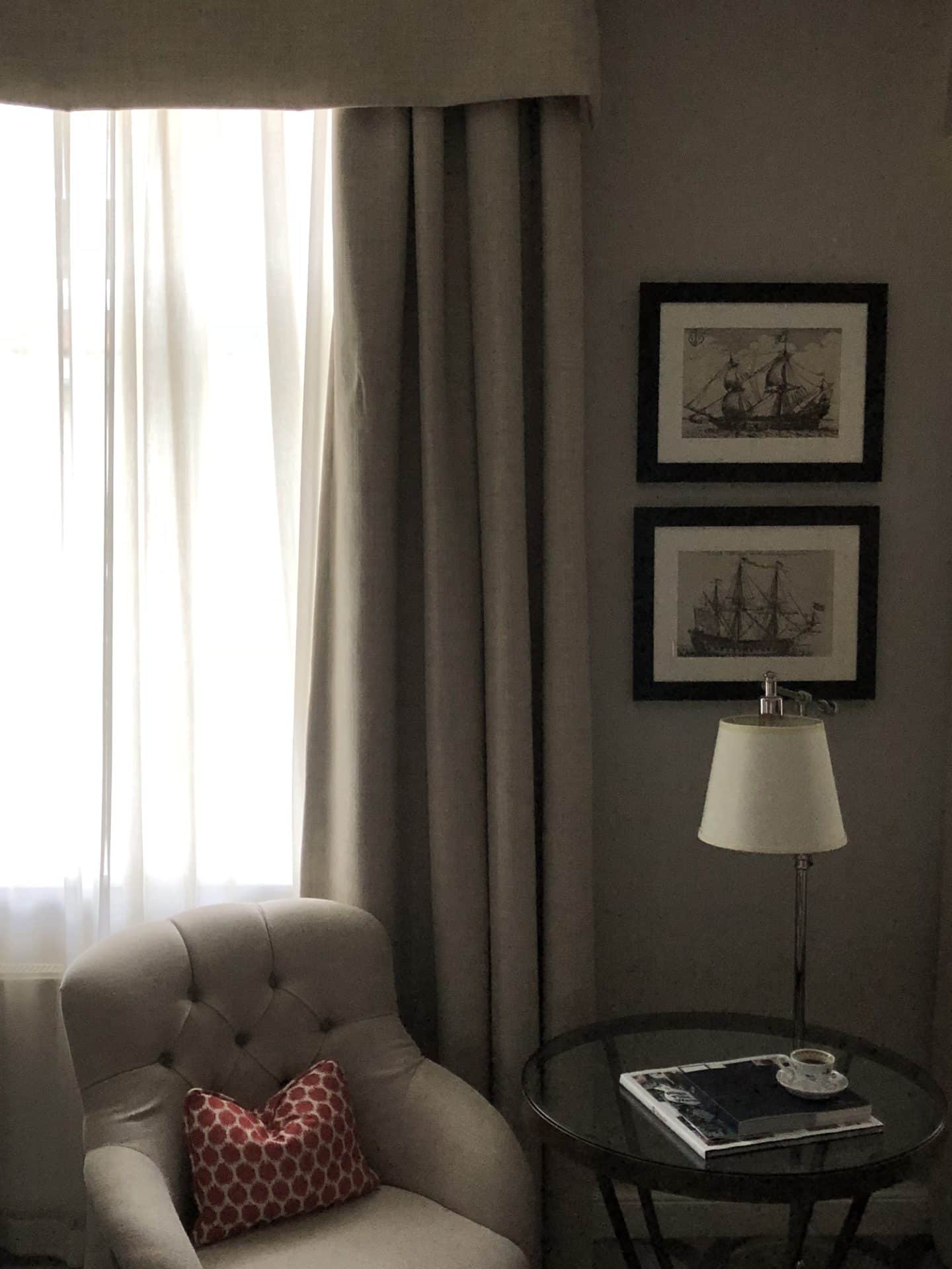 The Grand Palace Hotel Riga deluxe room with white table lamp, beige armchair and cream curtains 