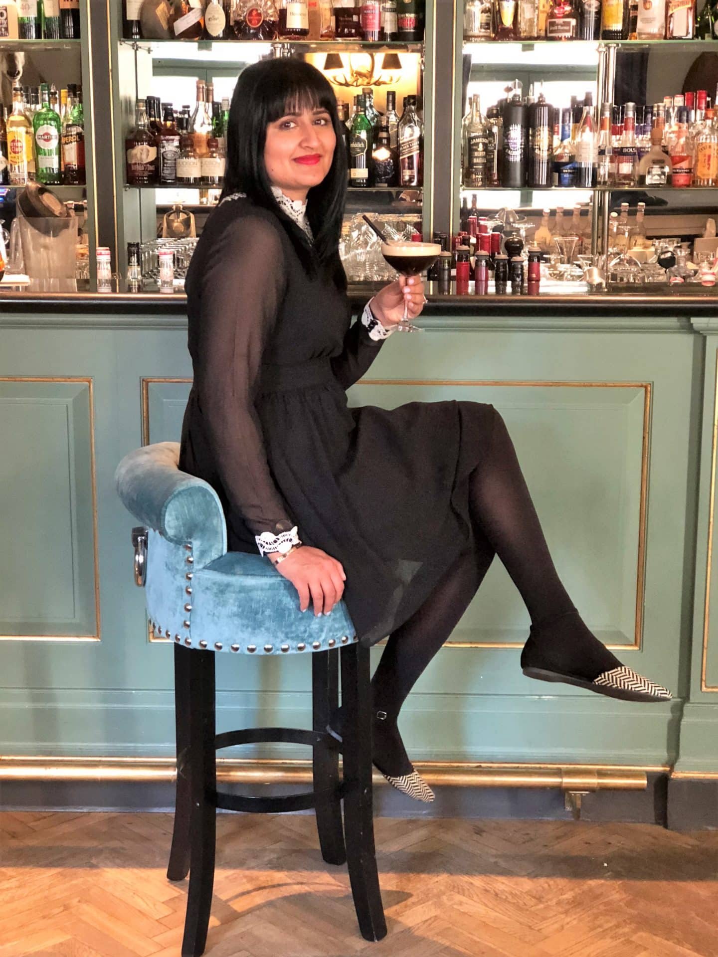 The Grand Palace Hotel Riga where Bejal is sitting at the bar with on a teal-coloured stool  with the bar background behind