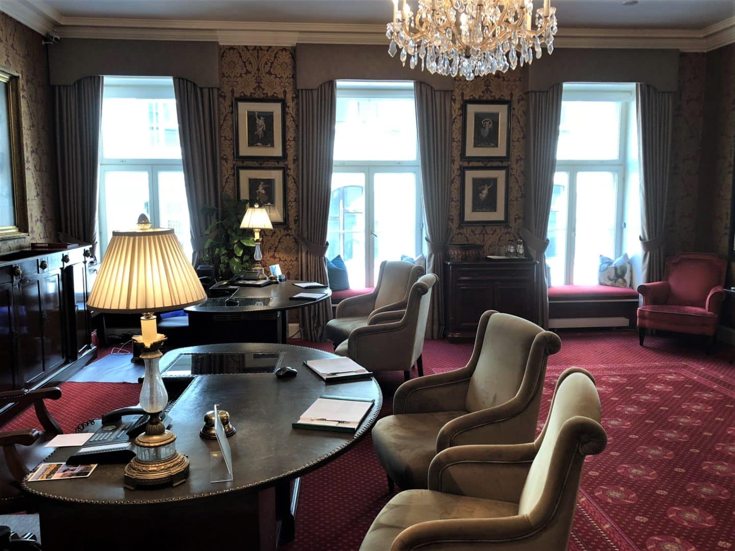 The Grand Palace Hotel Riga reception desk room with ornate chandelier and 4 chairs with dark brown furniture and red carpet