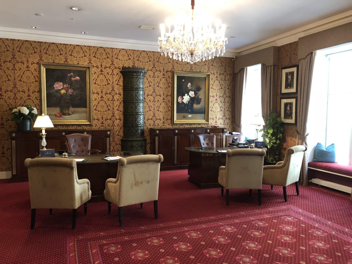 The Grand Palace Hotel Riga reception desk room with ornate chandelier and 4 chairs with dark brown furniture and red carpet