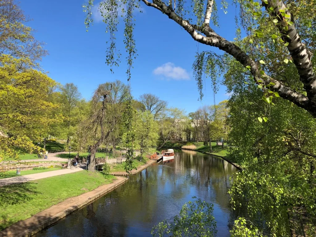 Boat coming down the river with foliage at eithr side in Bastejkalns Park, Riga