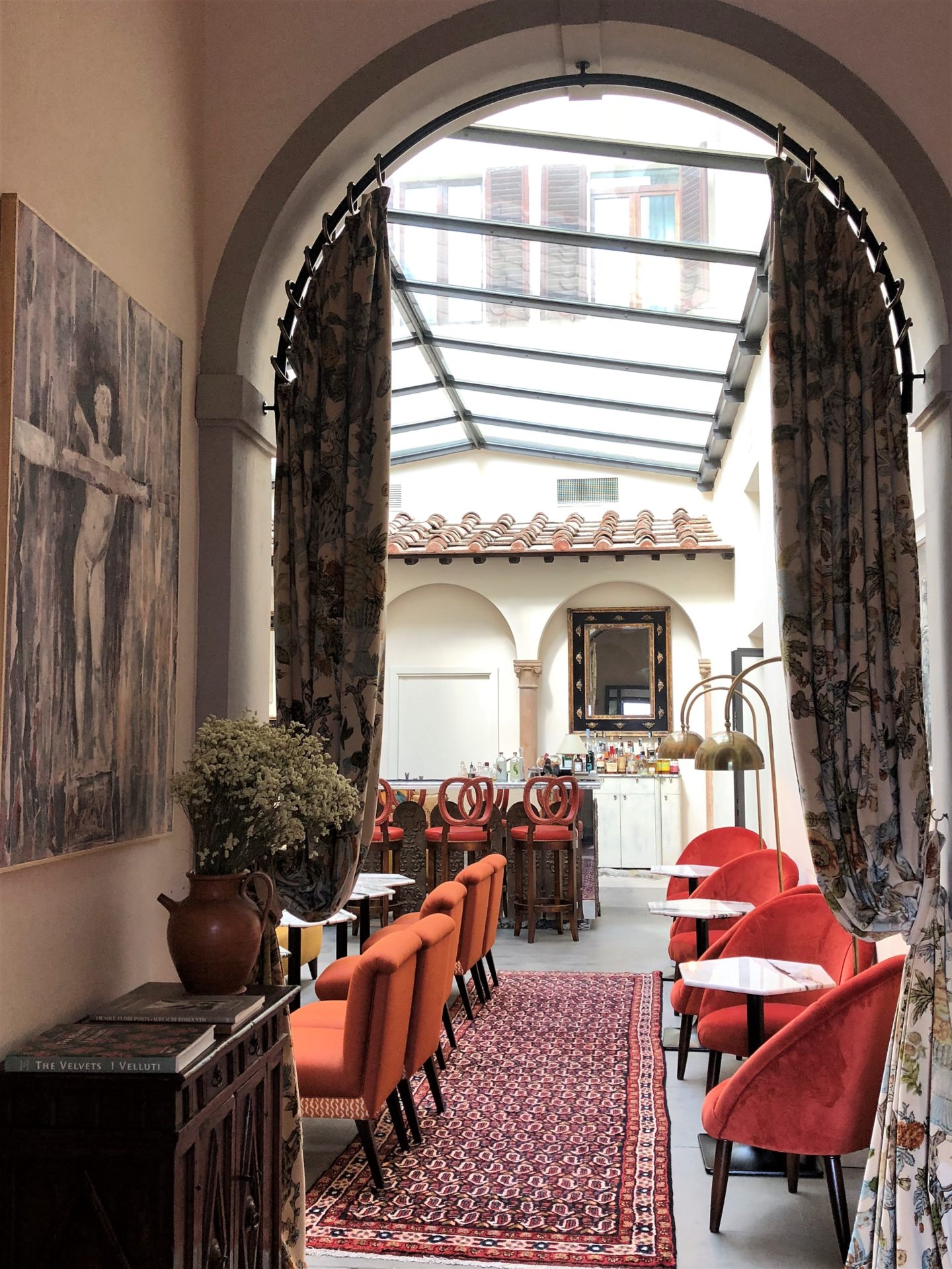 The archway into bar area lined with terracotta chairs, draped brown curtains and dark wood side boards.