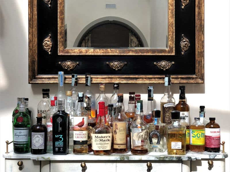 Marble topped shelf with spirits and liqueurs at the bat above which sits a black framed mirror. 