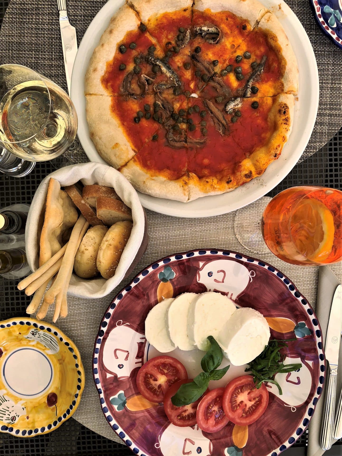 Mozzarella, bread sticks and pizza flat lay photo of Lunch at the pool area. An Aperol Spritz with a checked at underneath.
