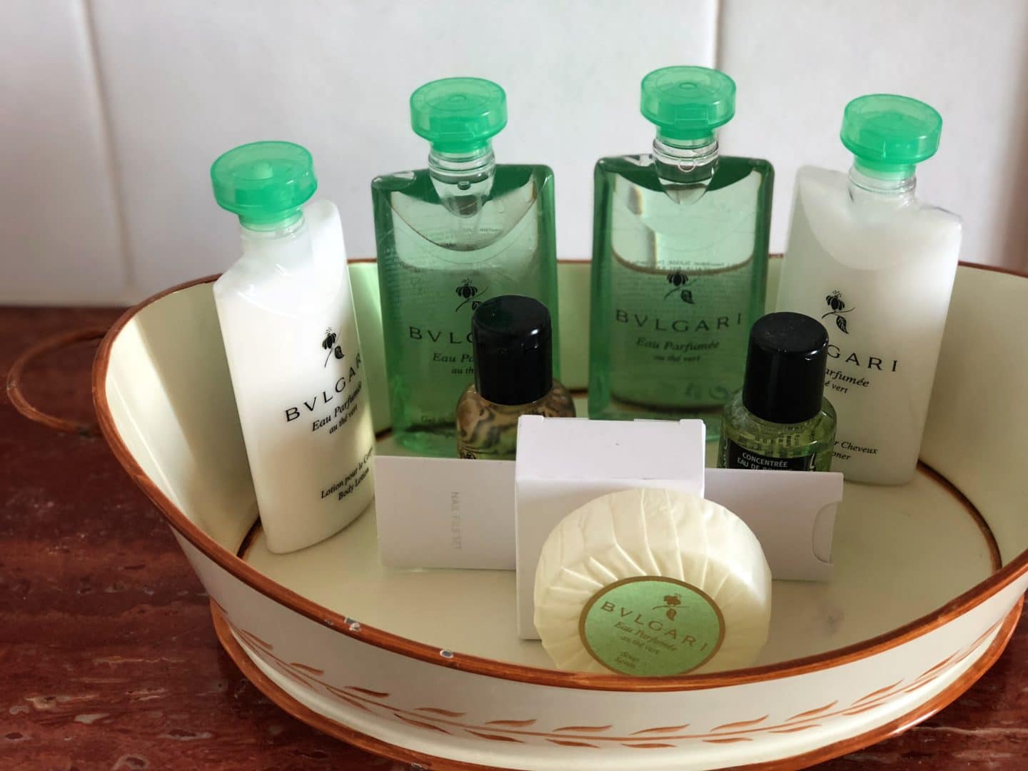 A white bowl with Bvlgari toiletries and soaps on a dark wood bench in the bathroom 