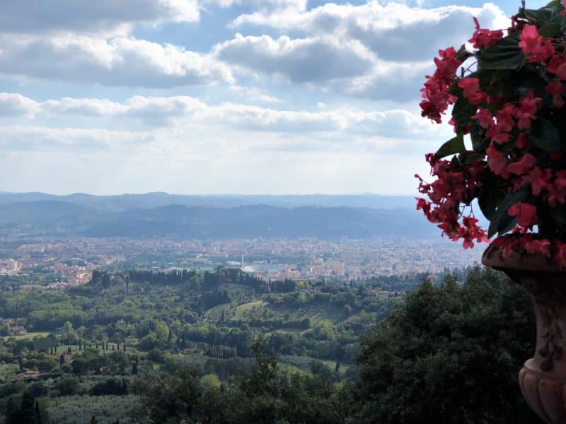 Belmond Villa San Michele: A stunning luxury hotel in Fiesole. View of Florence in the distance framed by the green lush hills of Fiesole. A potto the left of the imag eis filled with small pink flowers.
