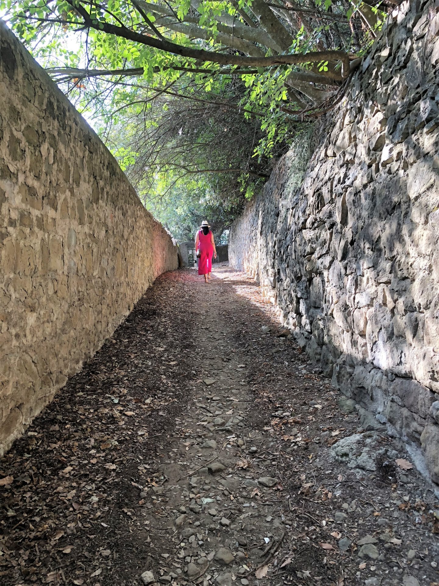 Bejal wearing a cerise pink jumpsuit walking down a gravel path with trees on either side. leading to the village of Fiesole.