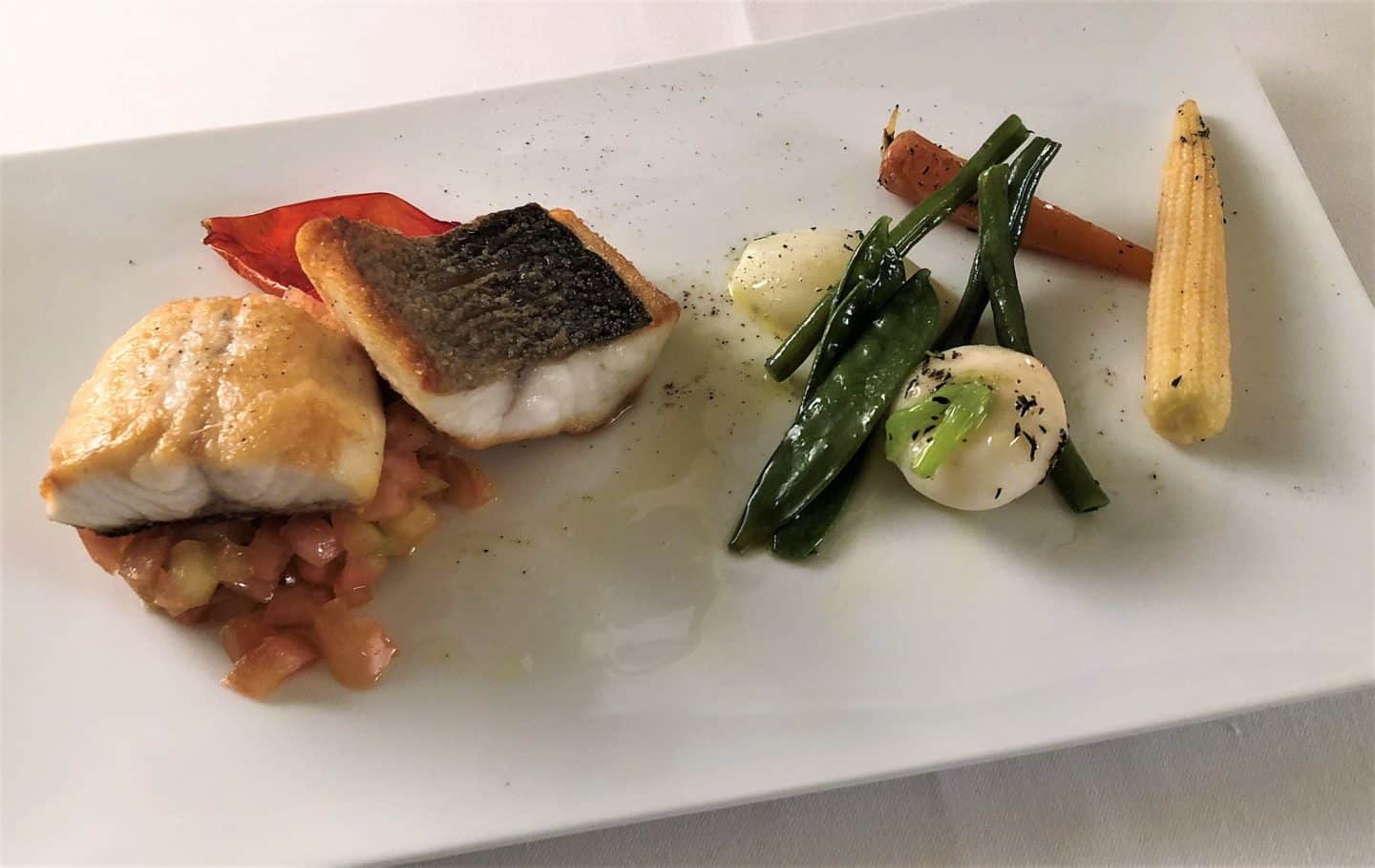 A Stunning luxury hotel in Fiesole: roasted Sea bass fillet with green tomatoes and thyme scented baby vegetables on a white oblong plate