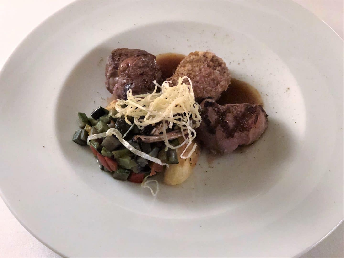 A Stunning luxury hotel in Fiesole: lamb; baby lamb chops grilled, coated in porcini powder and with breadcrumbs, served with stewed vegetable caponata and caramelised mint drops.served on a bright white plate.