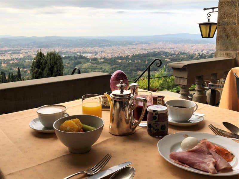 A stunning luxury hotel in Fiesole: coffee, orange juice, fruit, boiled eggs and ham laid out for breakfast with a view of Florence in the background at La Loggi restaurant.