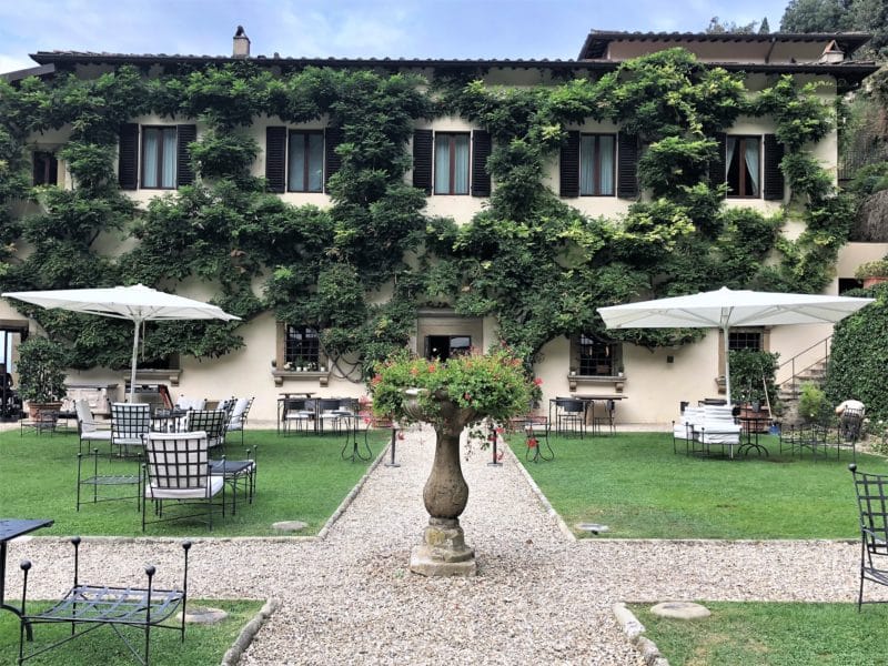 A stunning luxury hotel in Fiesole: The Loggia outdoorbar with wrought iron seats with cushions. Vases with flowers and garden parasols to keep the sun and rain off.