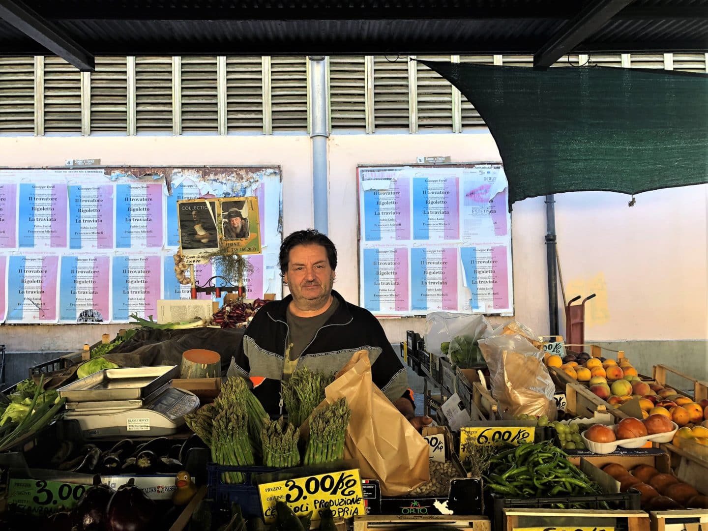 A market trader gentleman with loose fruit and vegetables in front of him as well as weighing scales at Mercato di Sant’Ambrogio in Florecne.