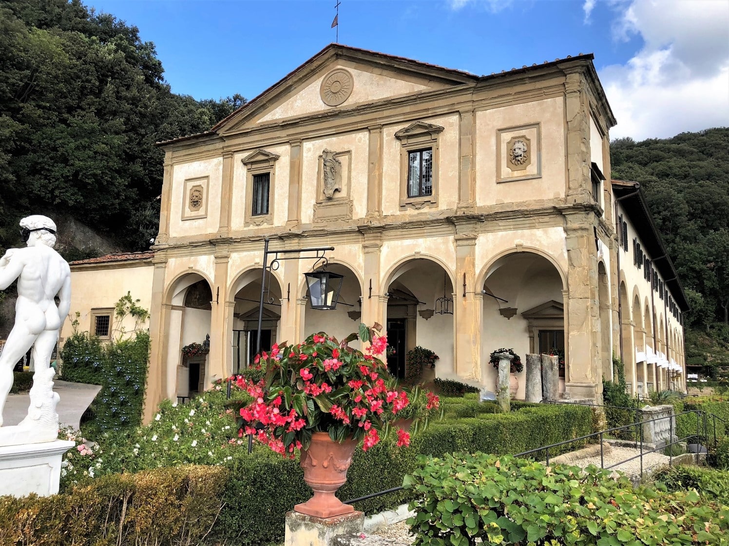 Belmond Villa San Michele: A stunning luxury hotel in Fiesole. the exterior of the front portion of the hotel from the gardens. In a traditional renaissance style with beige and dark wood panelling. The garden is filled with hedges and bougainvillea vases.