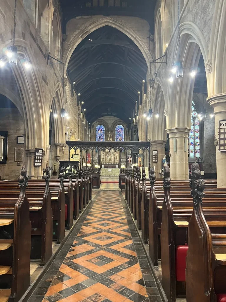 Aisle inside St Mary de Castro Church, Leicester. The pews are dark wood with the altar right in the background