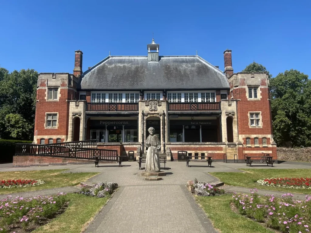 Cardinal Wolsey Statue at Abbey Park infront of Peppercorns cafe in a red brick building, surrounded by flower beds