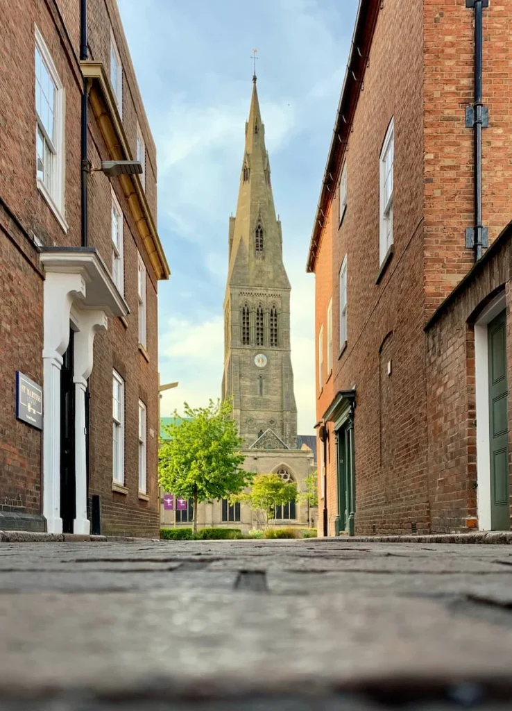 Cathedral spire from opposite Lane, called New Street. The spire lies in the centre of the image with Georgian brick buildings at either side and a cobbled stone street leading to the Cathedral