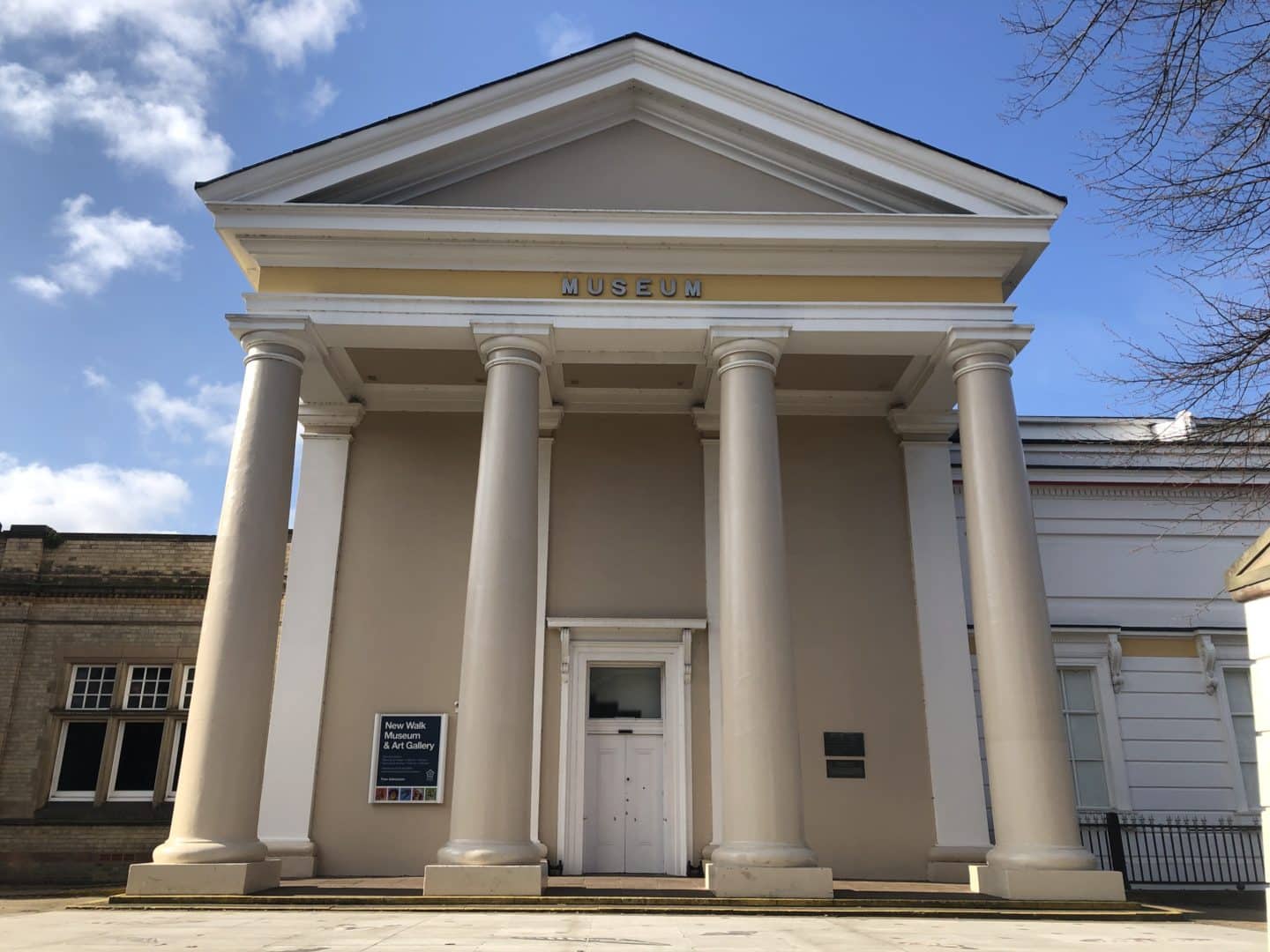 The white exterior of New Walk Museum and Art Gallery with 4 cream and beige pillars and white door. Behind the building is the bright blue summer sky.