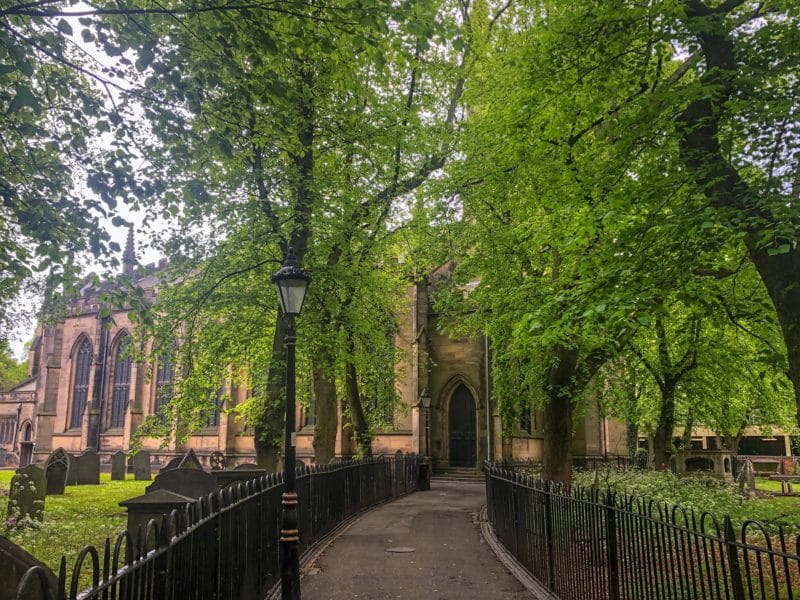 A Locals Guide to Historic Leicester A Locals Guide to Historic Leicester, St Georges Church on Orton Square with a path running through the middle. The church is covered up with green leaves of teh trees in summer.
