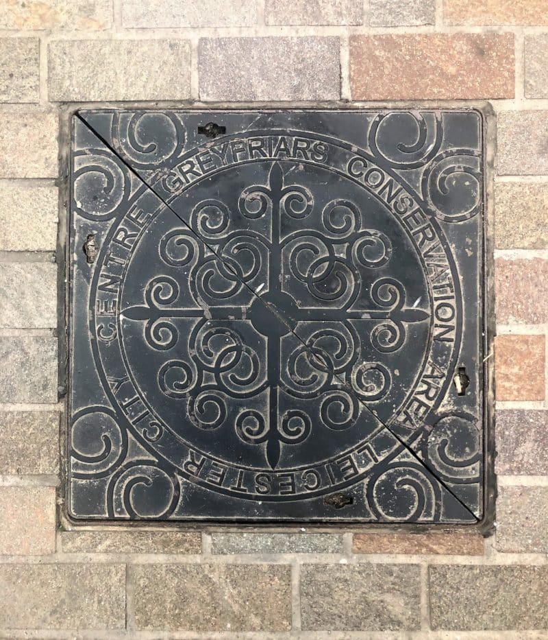 A Locals Guide to Historic Leicester A Grey Friars etched drain cover in medieval Leicester, surrounded by the tiled pavement.