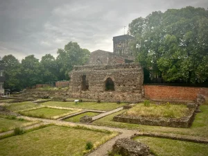 Jewry Wall Museum exterior with grass and low level wall on the main courtyard. The trees from St Nicholas Church surround the grey and beige stone wall, with a brick wall walkway to the side in this locals guide to historic Leicester
