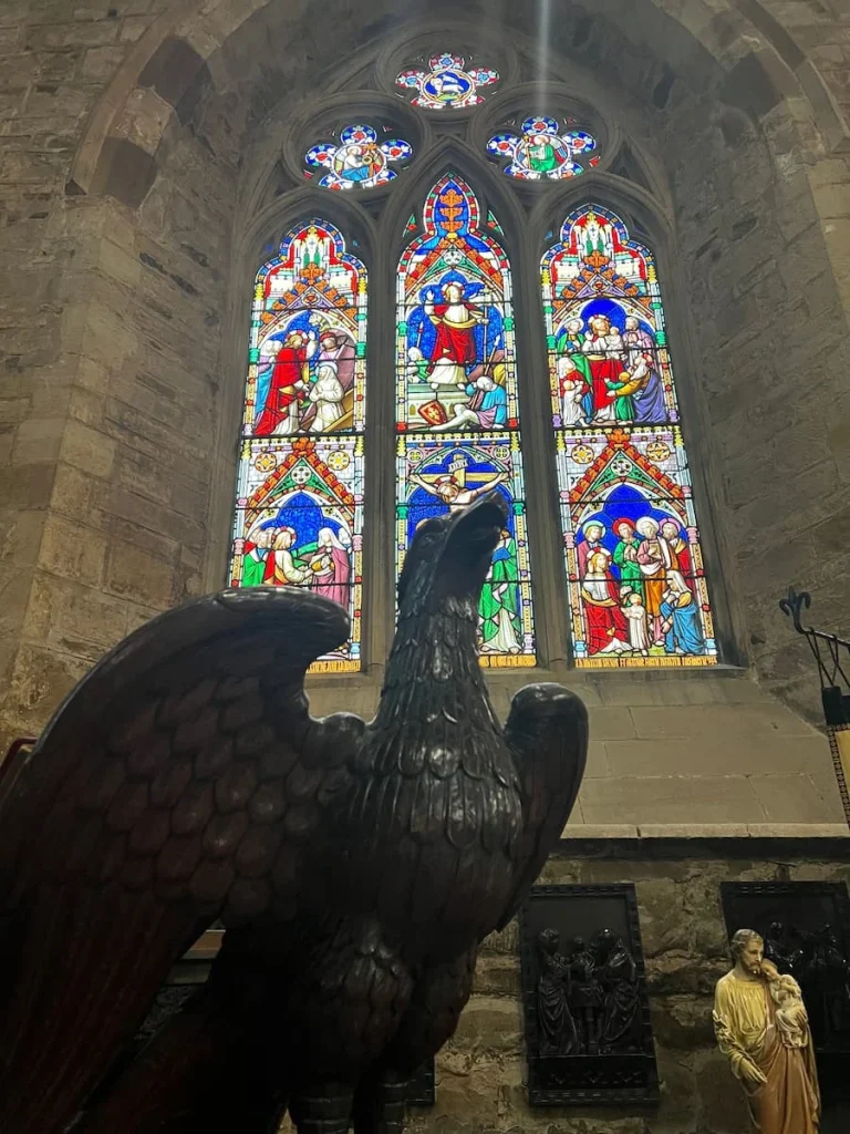 Stained glass window inside St Mary de Castro Church, Leicester with an eagle statue in front. The stained glass window in in hues of blue, red, tellow and green