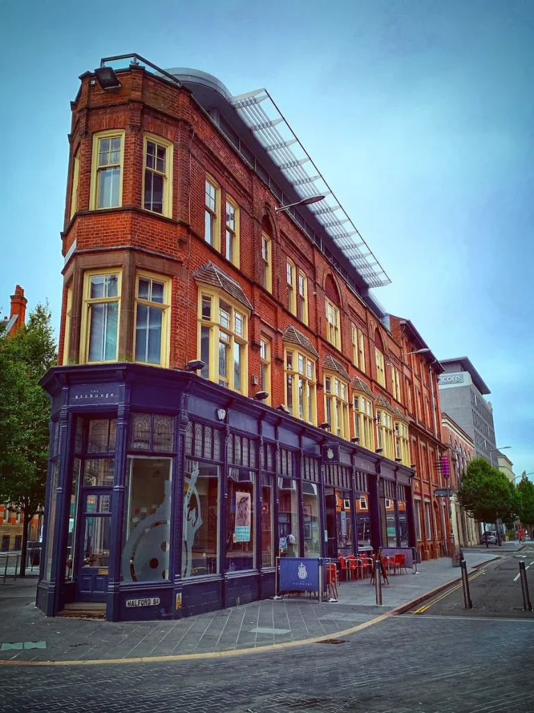 The Exchange Building side view with it's red brick structure and grey bar front with outdoor seating in Leicester's Cultural Quarter