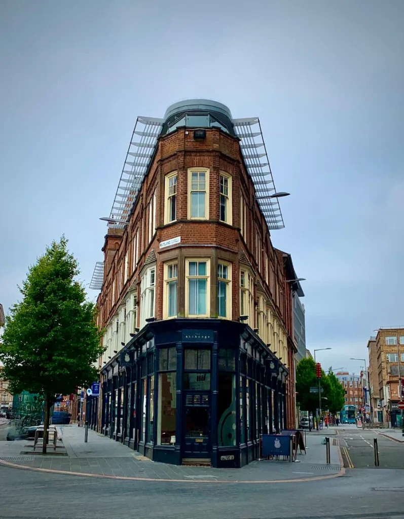the Exchange Building front view with a tree to the left and its red brick structure with grey bar front in Leicester's Cultural Quarter
