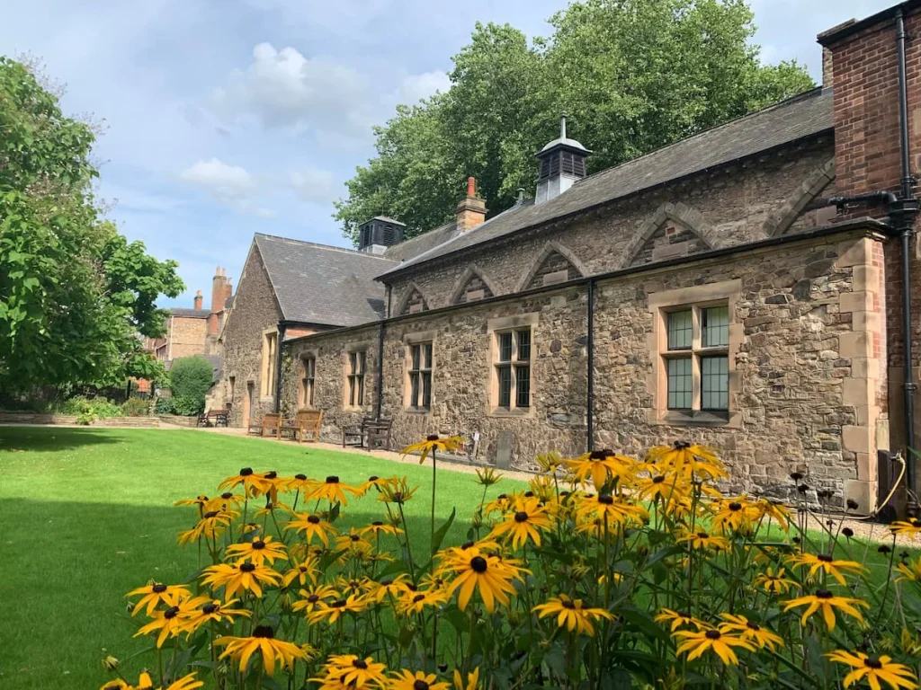 Trinity House Herb Garden but with the Trinity House stone building framed by the lawn and bright yellow daisies in Leicester